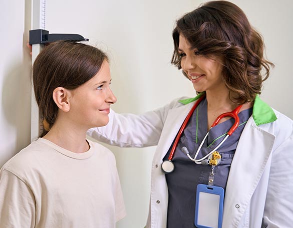 A young girl being measured for height by a smiling female doctor during a medical check-up.