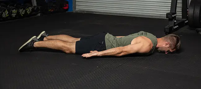 Brian Klepacky lying face down on a gym floor in a relaxed position, arms extended alongside his body.