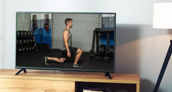 A TV screen displaying Brian performing a lunge exercise in a gym, set in a
                modern living room.