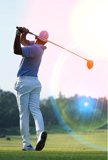A golfer mid-swing on a sunny day, with a vibrant lens flare in the background.